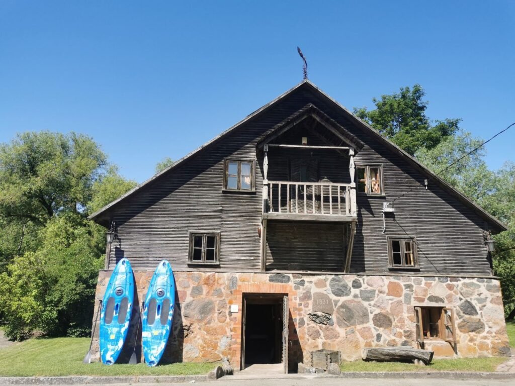 Senas malūnas – medinis fasadas su balkonu ir akmeniniu pamatu, prie sienos irklentės